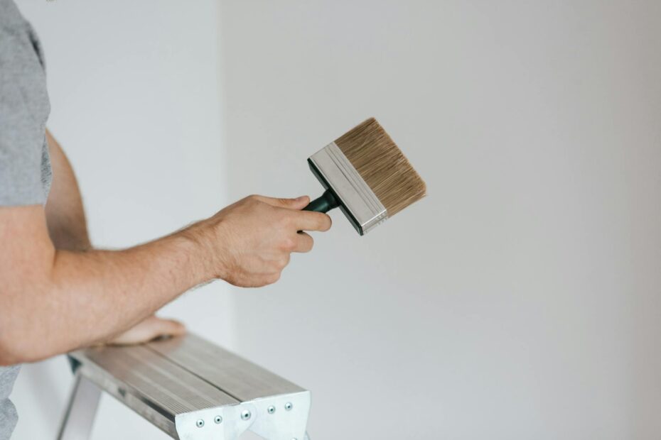 Side view of crop faceless painter in casual clothes holding paintbrush while leaning on stepladd... (Photo by Anete Lusina on Pexels)