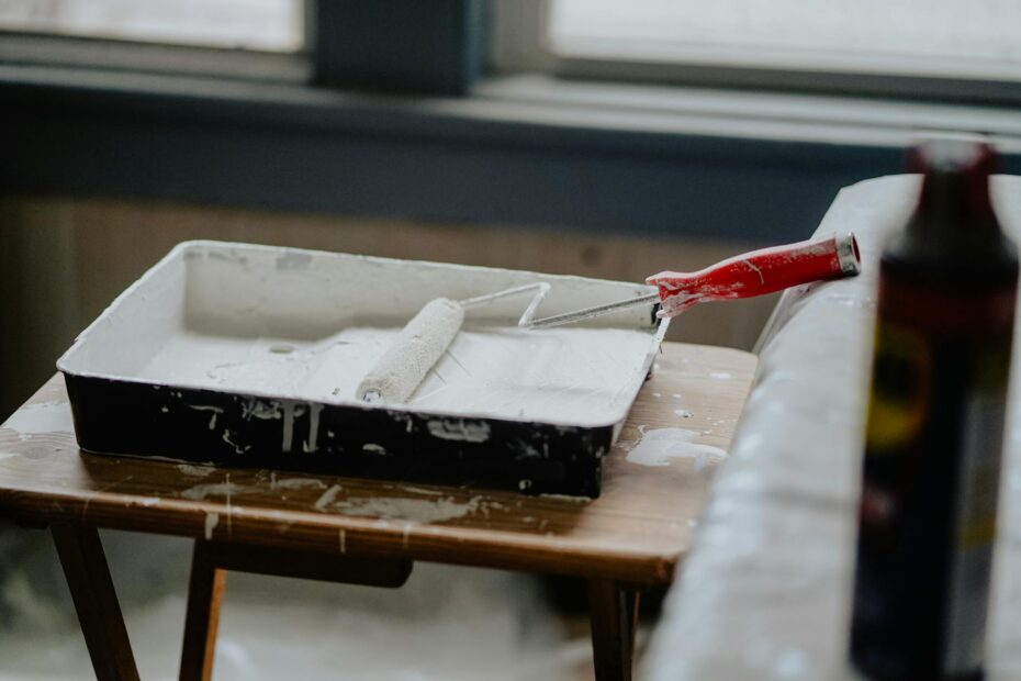 A paint roller and tray with white paint on a wooden table, indicating a renovation work. (Photo by Karl Solano on Pexels)
