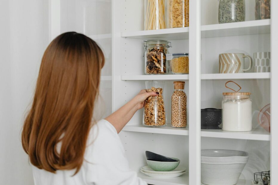 Woman arranging jars on pantry shelves for organized food storage. (Photo by www.kaboompics.com on Pexels)