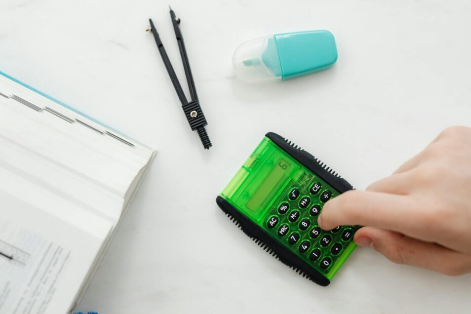 Close-up of a hand using a green calculator with stationery for studies or business calculations. (Photo by www.kaboompics.com on Pexels)