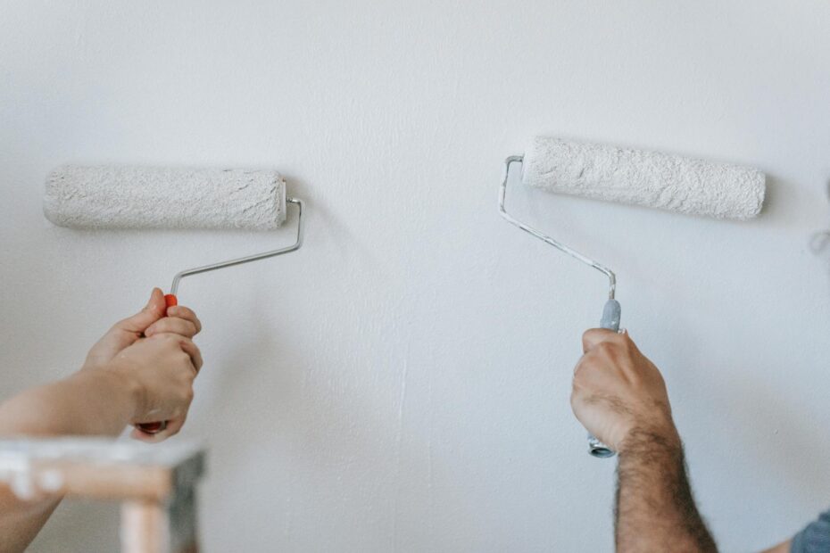 Close-up of two individuals painting a wall with paint rollers indoors. (Photo by Blue Bird on Pexels)