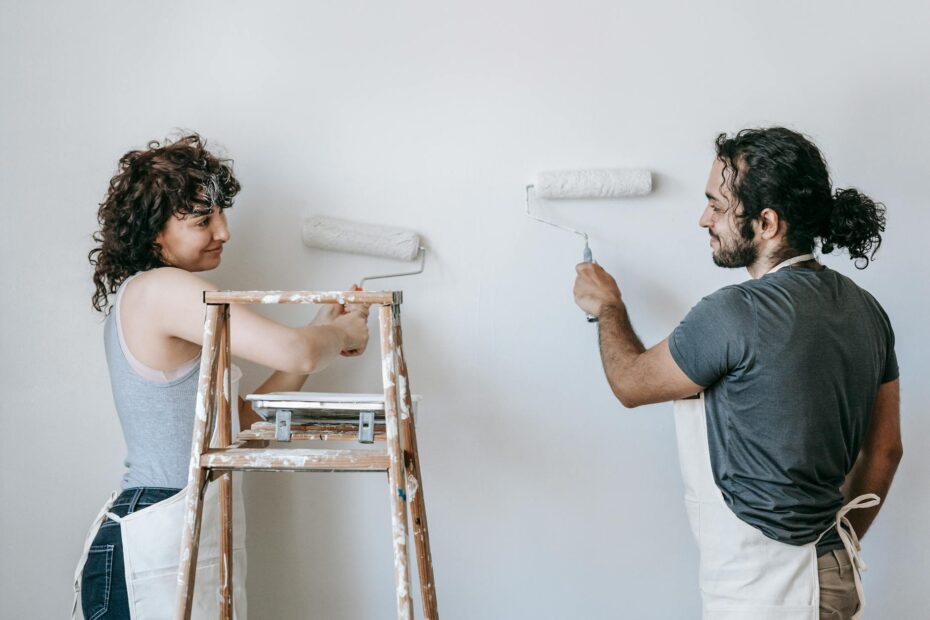 Cheerful adult ethnic couple in aprons looking at each other while painting wall with rollers dur... (Photo by Blue Bird on Pexels)