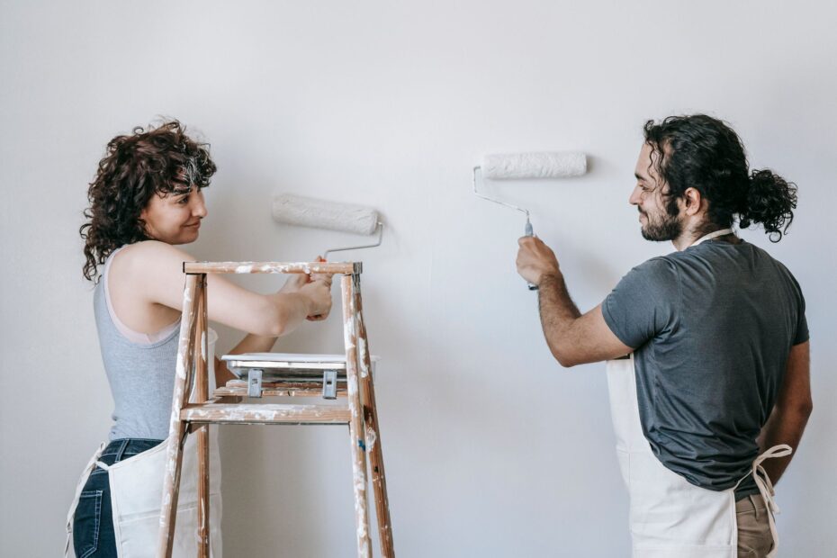 Cheerful adult ethnic couple in aprons looking at each other while painting wall with rollers dur... (Photo by Blue Bird on Pexels)